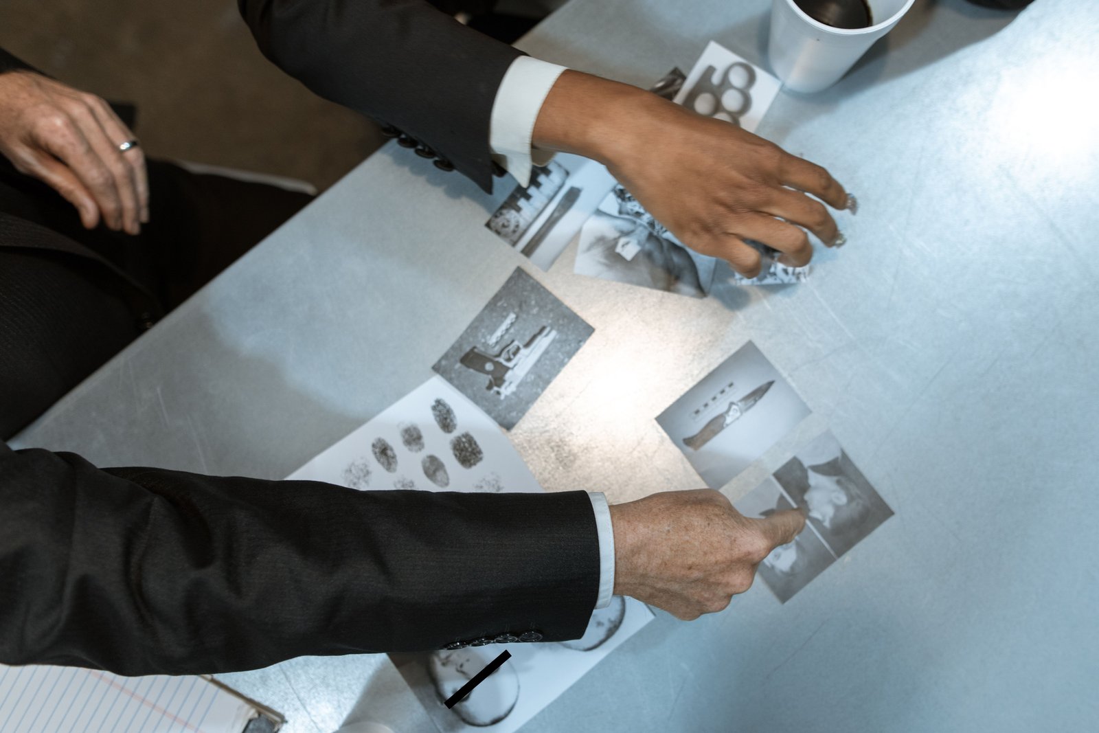 Detetives revisam fotos de evidências e impressões digitais sobre uma mesa, referente a indivíduo intimado para depor na delegacia